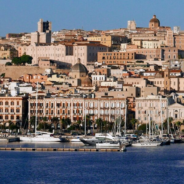 Vue du port avec bateaux et maisons historiques sur une colline ensoleillée.
