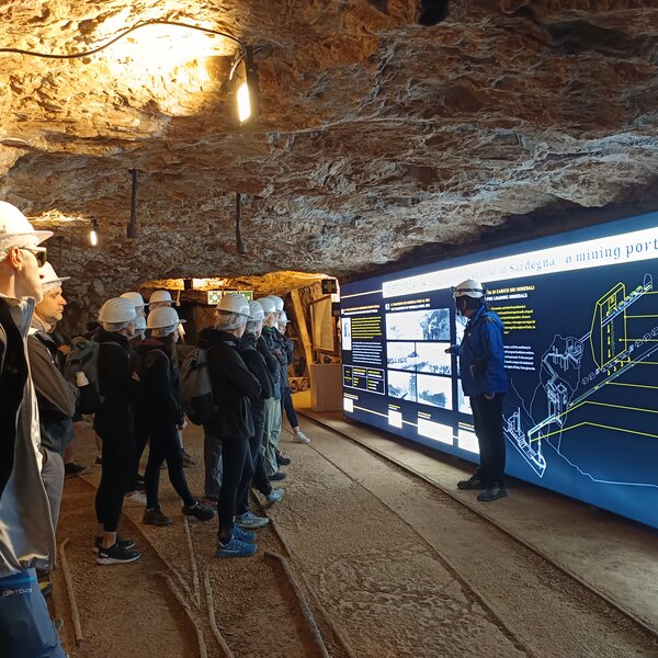Group wearing mining helmets listens to guide in underground tunnel.