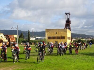 Group of mountain bikers riding on grass near an industrial building.