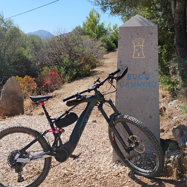 Electric bike leaning on a milestone with Buon Cammino inscription on dirt path
