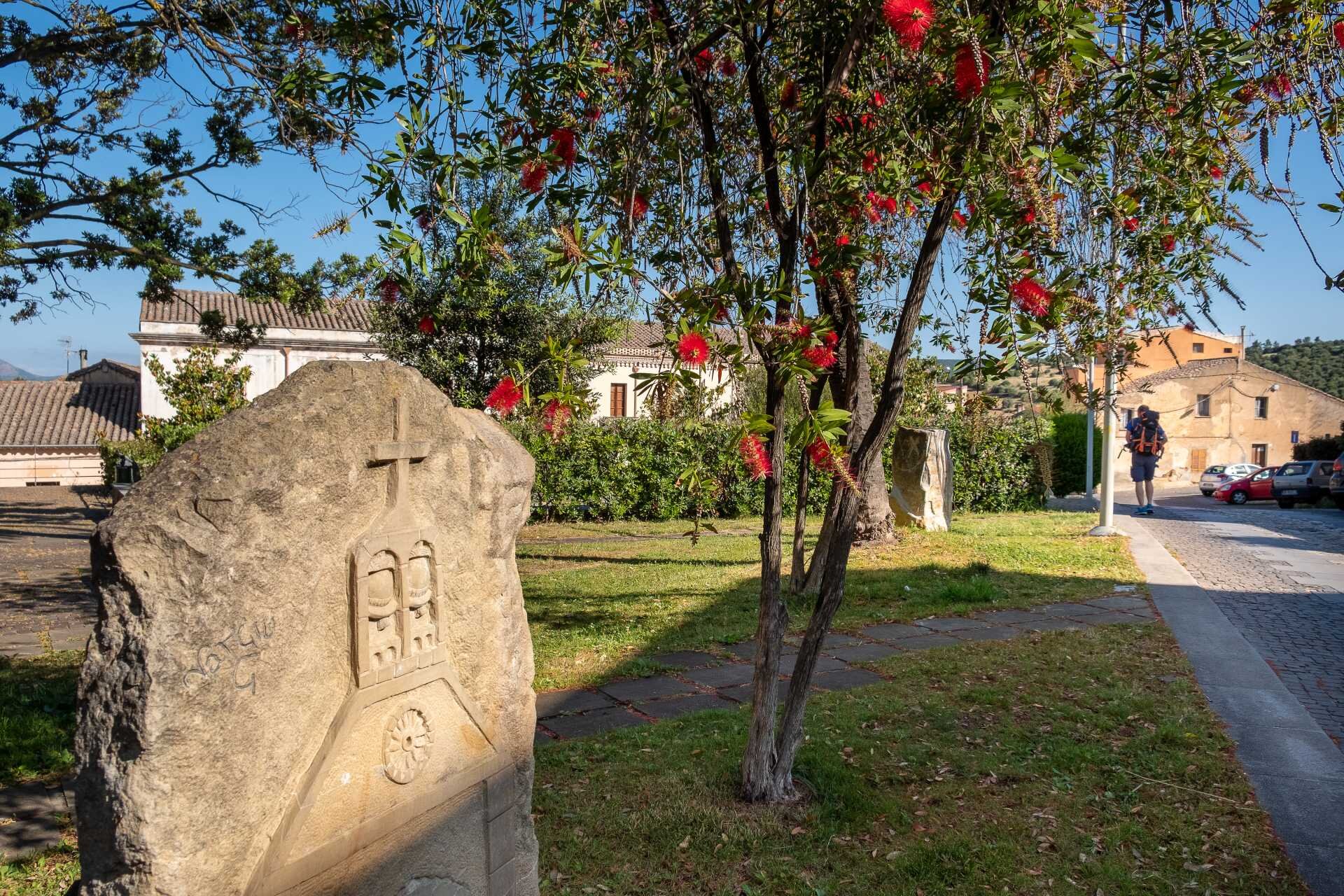 Steingrabstein mit religiösen Gravuren in einem sonnigen Garten mit blühendem Baum.