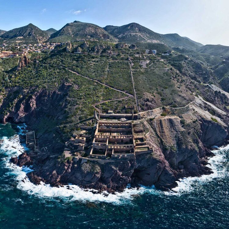 Veduta aerea di antiche rovine su una scogliera verde vicino al mare agitato.