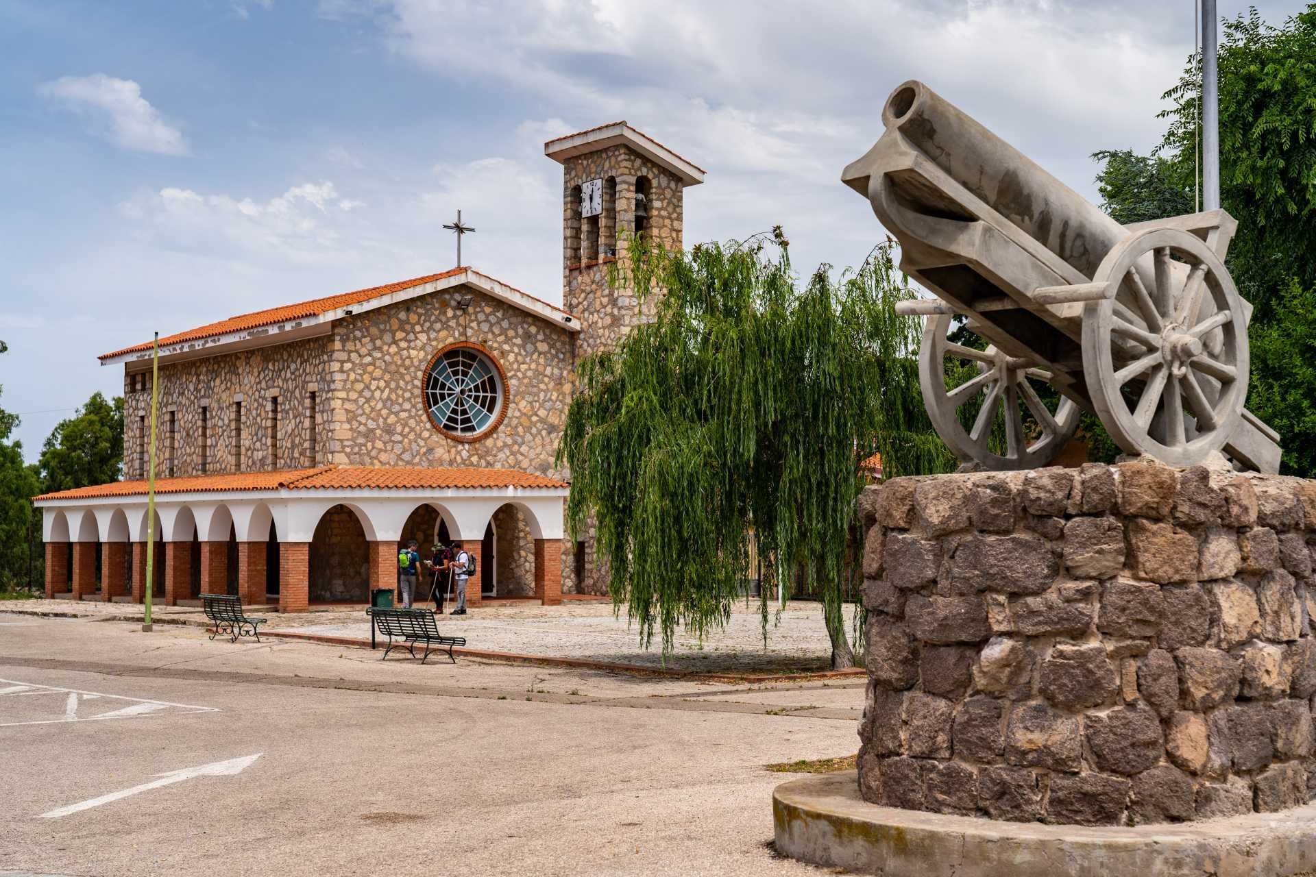 Stone church with bell tower, tree, and historic cannon in the foreground