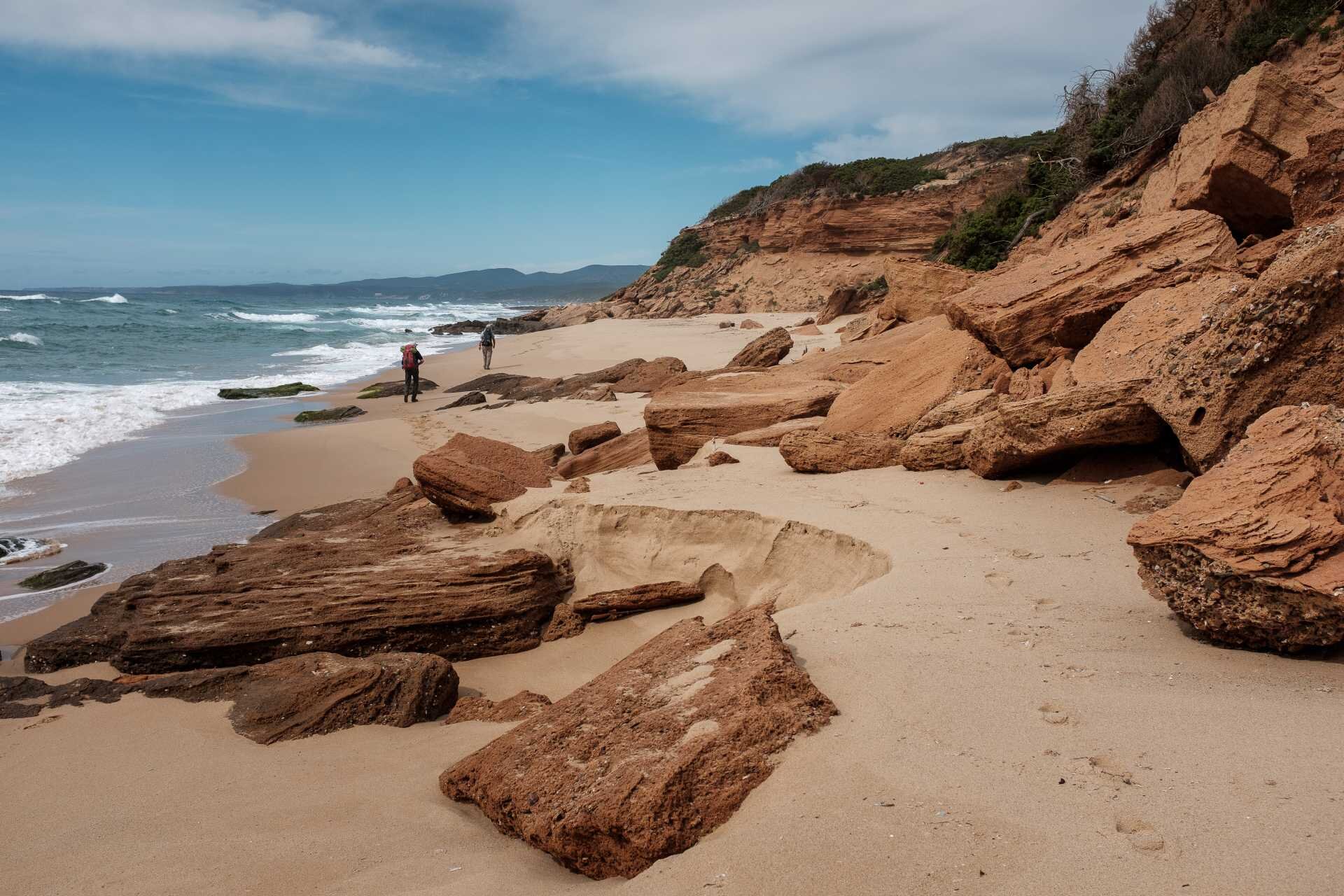 Rocky beach with two people walking near the sea under a partly cloudy sky