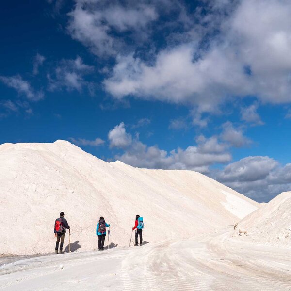 Three hikers with backpacks walking on white terrain under a cloudy sky.
