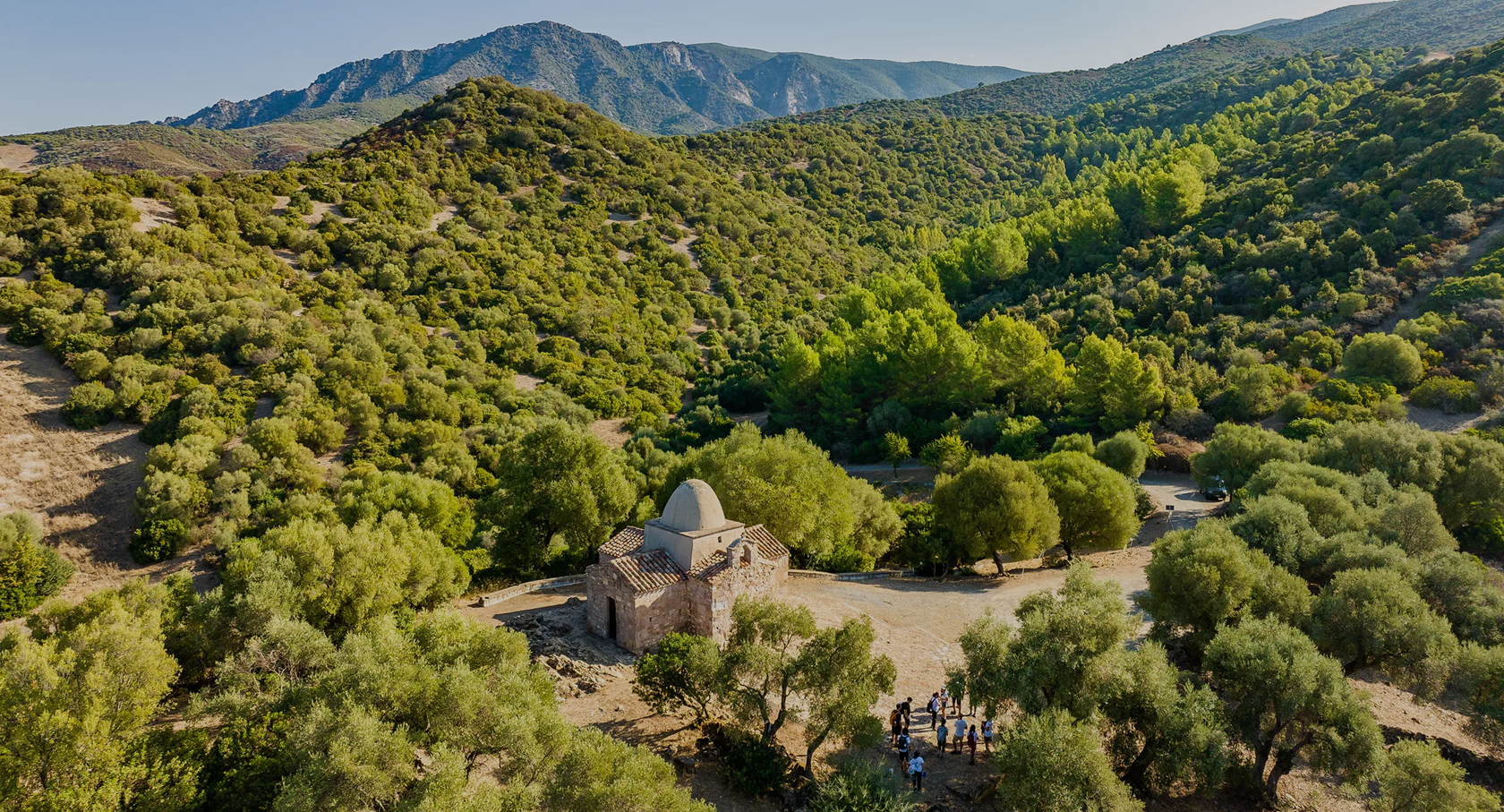 Petite église en pierre entourée d'arbres et de collines vertes.