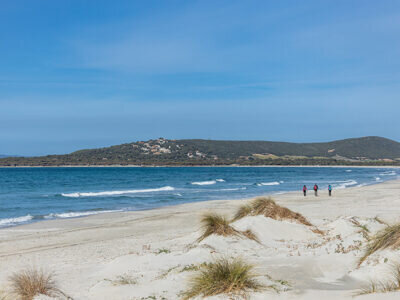 Plage de sable avec dunes et trois personnes marchant près de la mer.