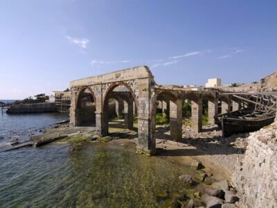 Ruines d'un ancien bâtiment avec arches au bord de la mer et bateau abandonné.