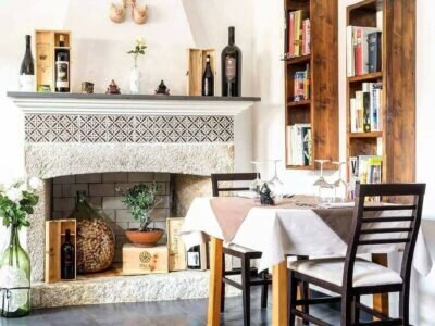 Salle à manger rustique avec cheminée, table dressée et étagères en bois.