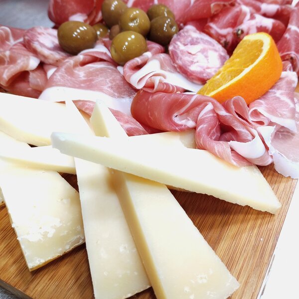 Tranches de fromage, charcuterie, olives vertes et tranche d'orange sur planche en bois