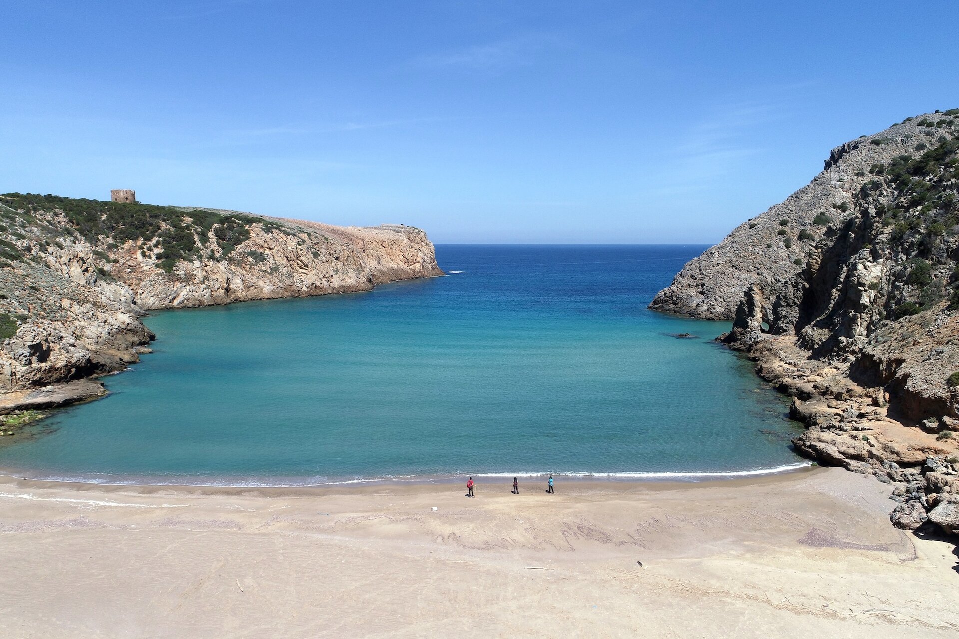 Calm beach with three people and turquoise sea between two rocky cliffs