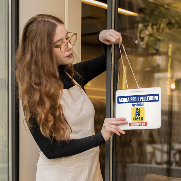 Woman with glasses hangs sign offering free water for pilgrims