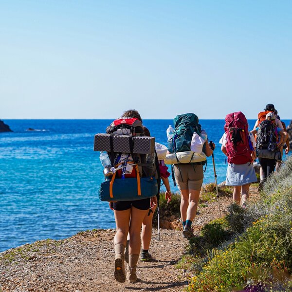 Group of hikers with backpacks walking on a sunny coastal trail.