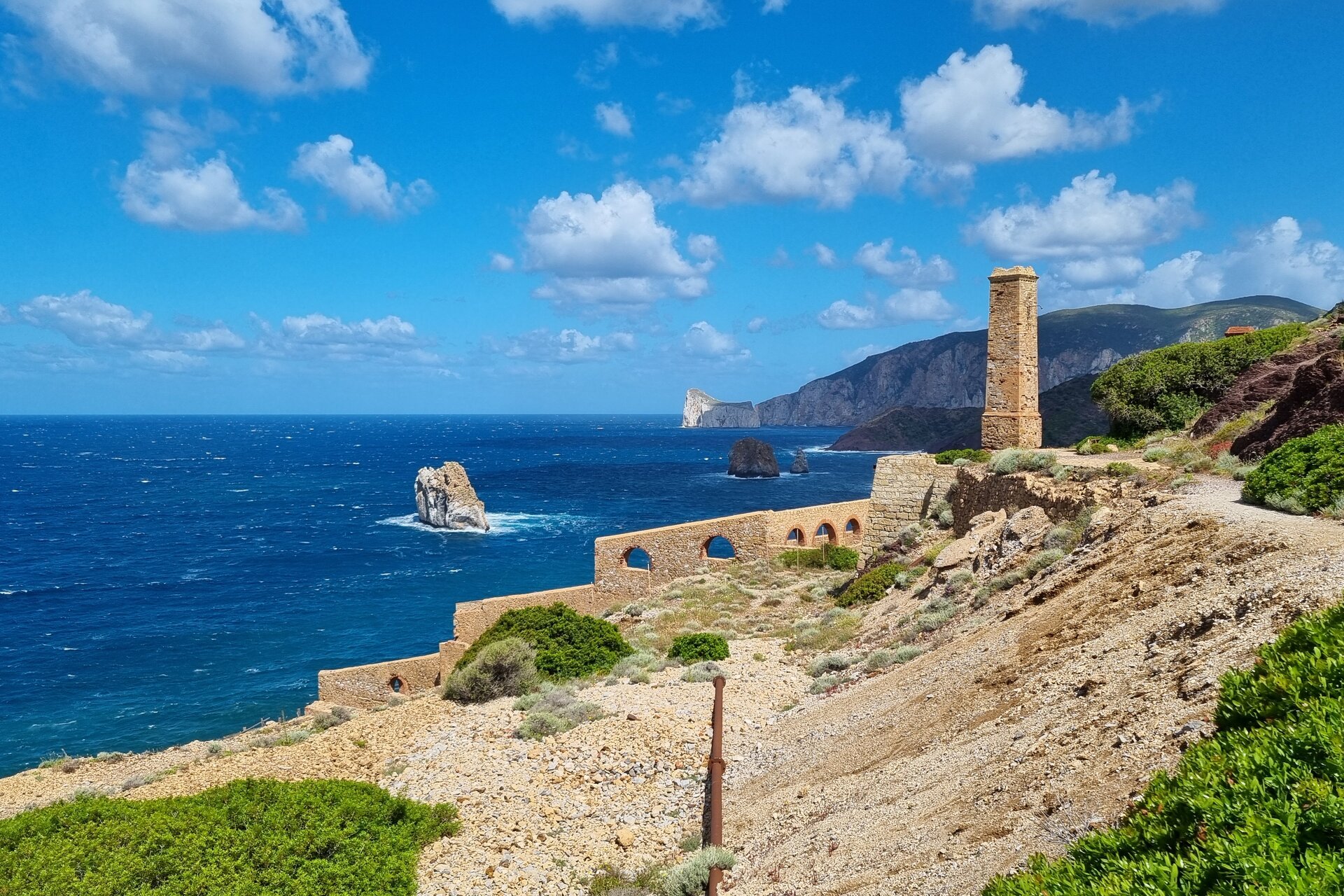 Ruderi storici su scogliera con vista mare e cielo azzurro con nuvole.
