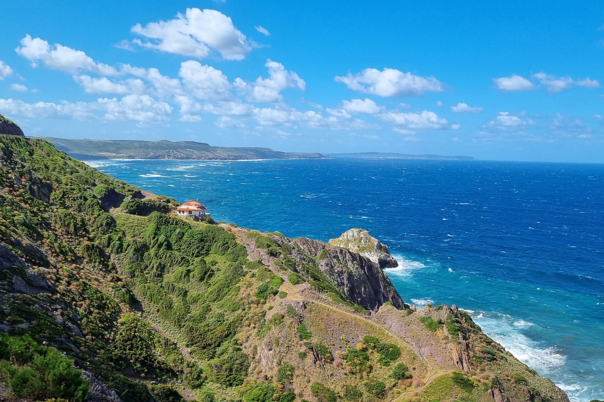 Côte rocheuse avec verdure et maison près de la mer bleue sous ciel bleu